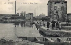 Carte postale ancienne en noir et blanc montrant le canal du Gier à Givors et les Usines Prénat. Dans le fonds on distingue les cheminées des usines desquelles sortent des panaches de fumée. À droite de l'image, sur les quais, il y a des enfants qui regardent la personne qui prend la photo. Au tout premier plan se trouve une barque en bois.