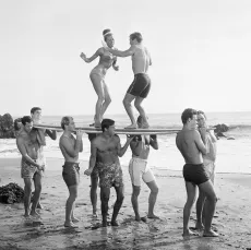 Image représentant des hommes et des femmes sur la plage en train de danser sur un surf